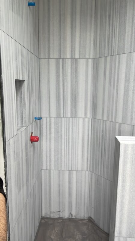 Marble-look porcelain shower walls being set with levelling clips before grout