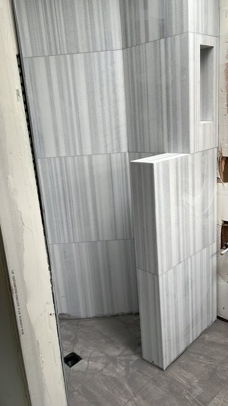 Striated marble-look porcelain shower with a tiled built-in bench being installed