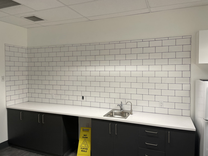 Staff kitchenette fit-out with hand-set ceramic subway tile backsplash, dark-grout joints and a seamless solid-surface counter.