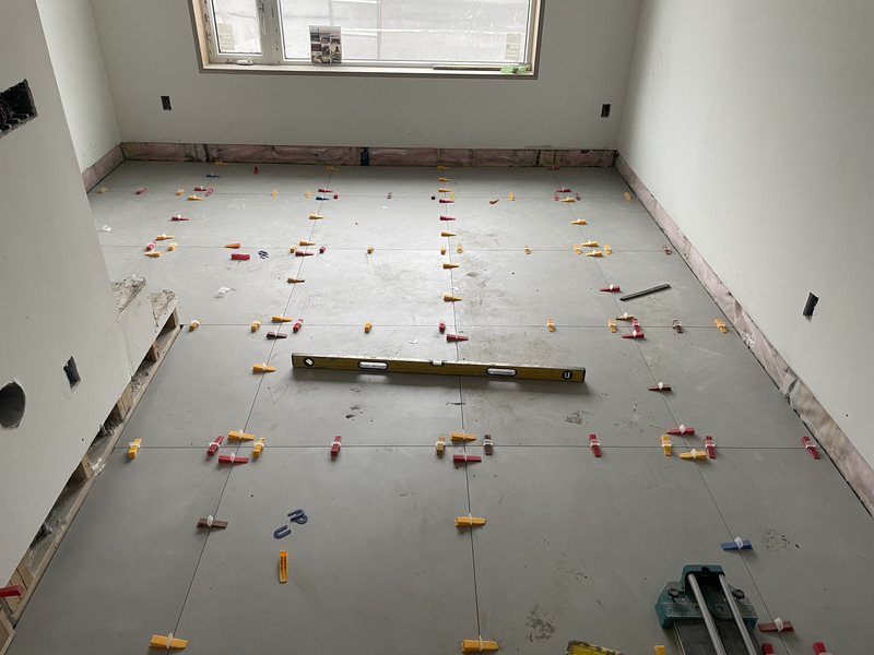 Large-format floor tile dry-laid and checked with a spirit level and leveling clips to plan grout lines before setting