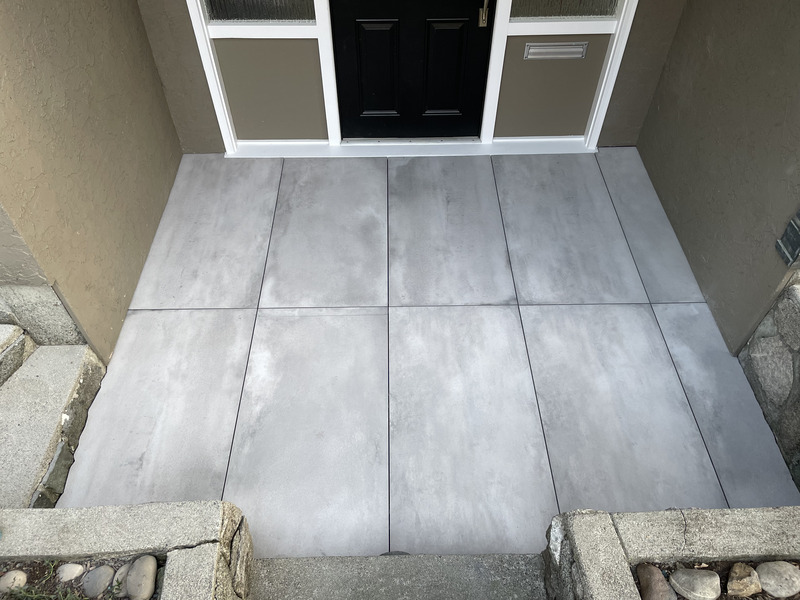 Large-format porcelain paver terrace and entry landing over a graded exterior slab, laid with tight joints and drainage fall.