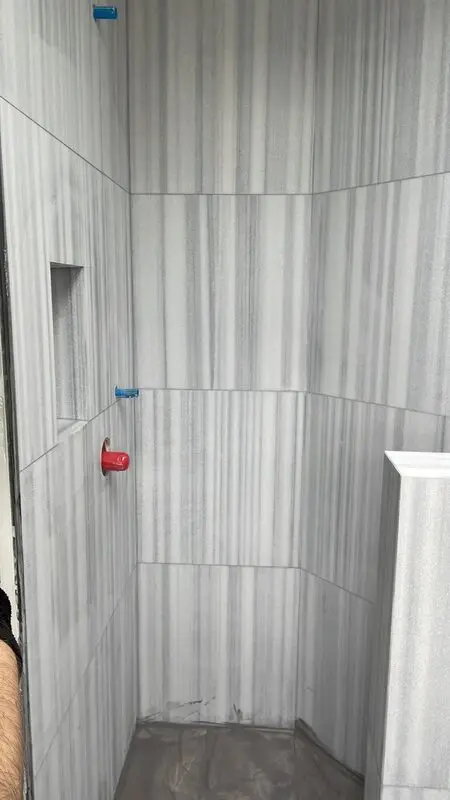 Marble-look porcelain shower walls being set with levelling clips before grout