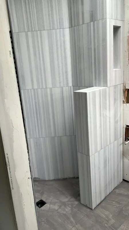 Striated marble-look porcelain shower with a tiled built-in bench being installed