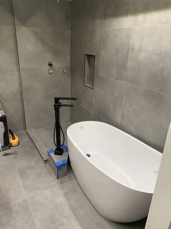 Freestanding soaker tub and matte black filler on newly laid concrete-look porcelain