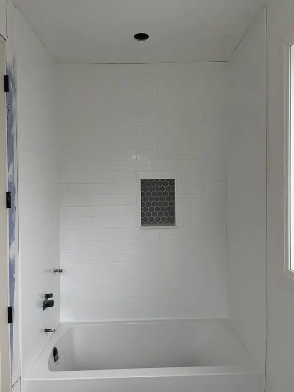 Glossy white subway tile tub surround with a recessed hexagon mosaic niche