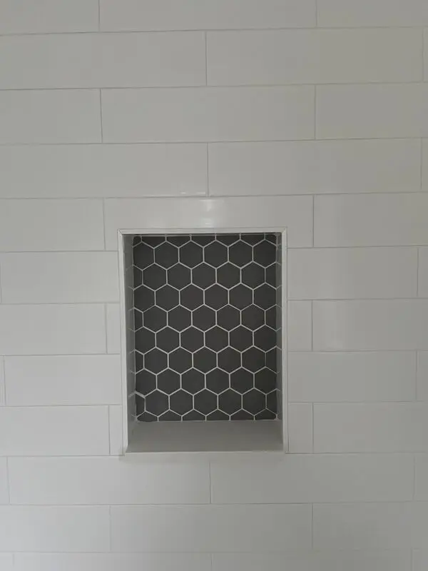 Close-up of a grey hexagon mosaic shower niche framed in white subway tile