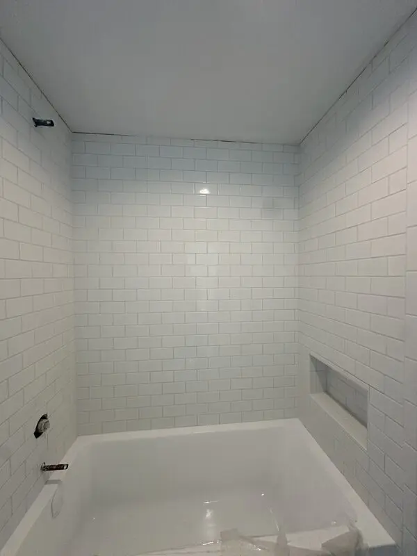 Full-height white subway tile shower over tub with recessed soap niche