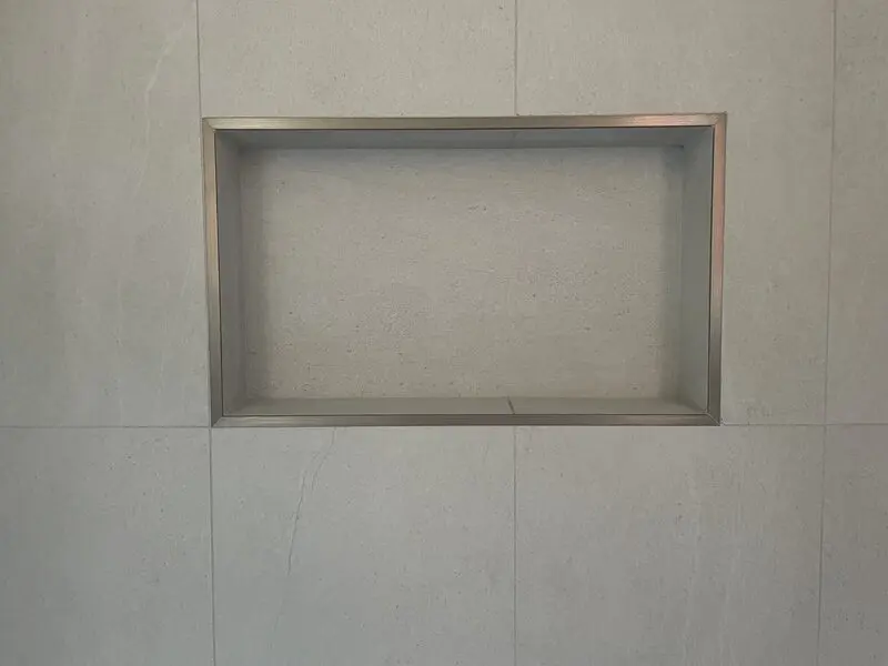 Recessed shower niche in soft white large-format porcelain with slim metal edge trim