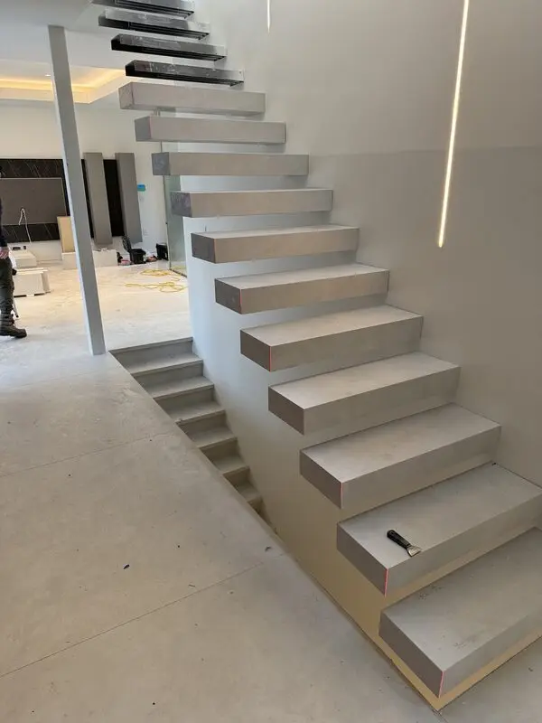 Cantilevered porcelain-clad floating stair treads beside a frameless glass railing