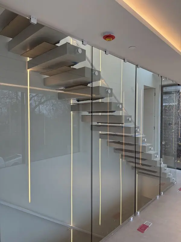Floating stone-look treads lit by warm cove lighting behind a glass balustrade