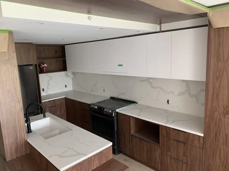 Pale quartz counters and matching full-height slab backsplash in a walnut kitchen
