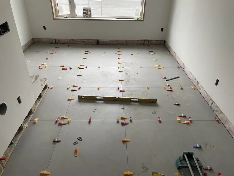 Large-format floor tile dry-laid and checked with a spirit level and leveling clips to plan grout lines before setting