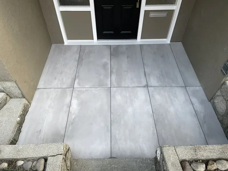 Grey concrete-look large-format porcelain pavers set as an entry landing with tight joints between granite kerb stones