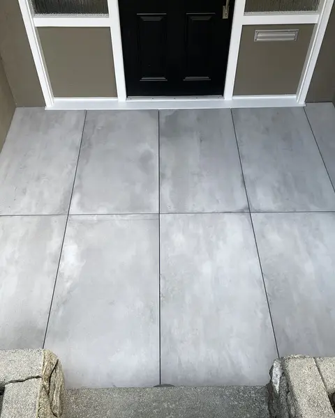 Grey concrete-look large-format porcelain pavers set as an entry landing with tight joints between granite kerb stones