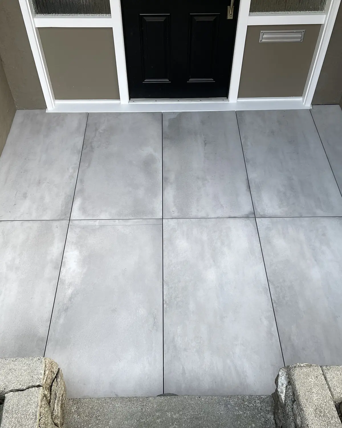 Grey concrete-look large-format porcelain pavers set as an entry landing with tight joints between granite kerb stones