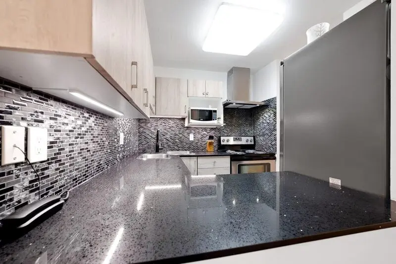 Polished granite counter run with undermount sink and glass mosaic backsplash